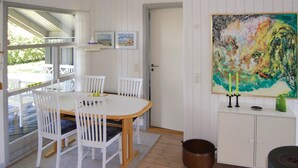 A dining area with a white table and chairs, a painting on the wall, and a view through the window.