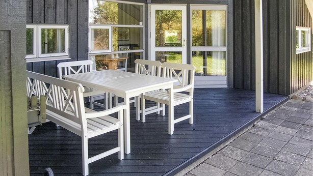 A covered outdoor seating area with a table and chairs, large windows, and a door leading to a garden.