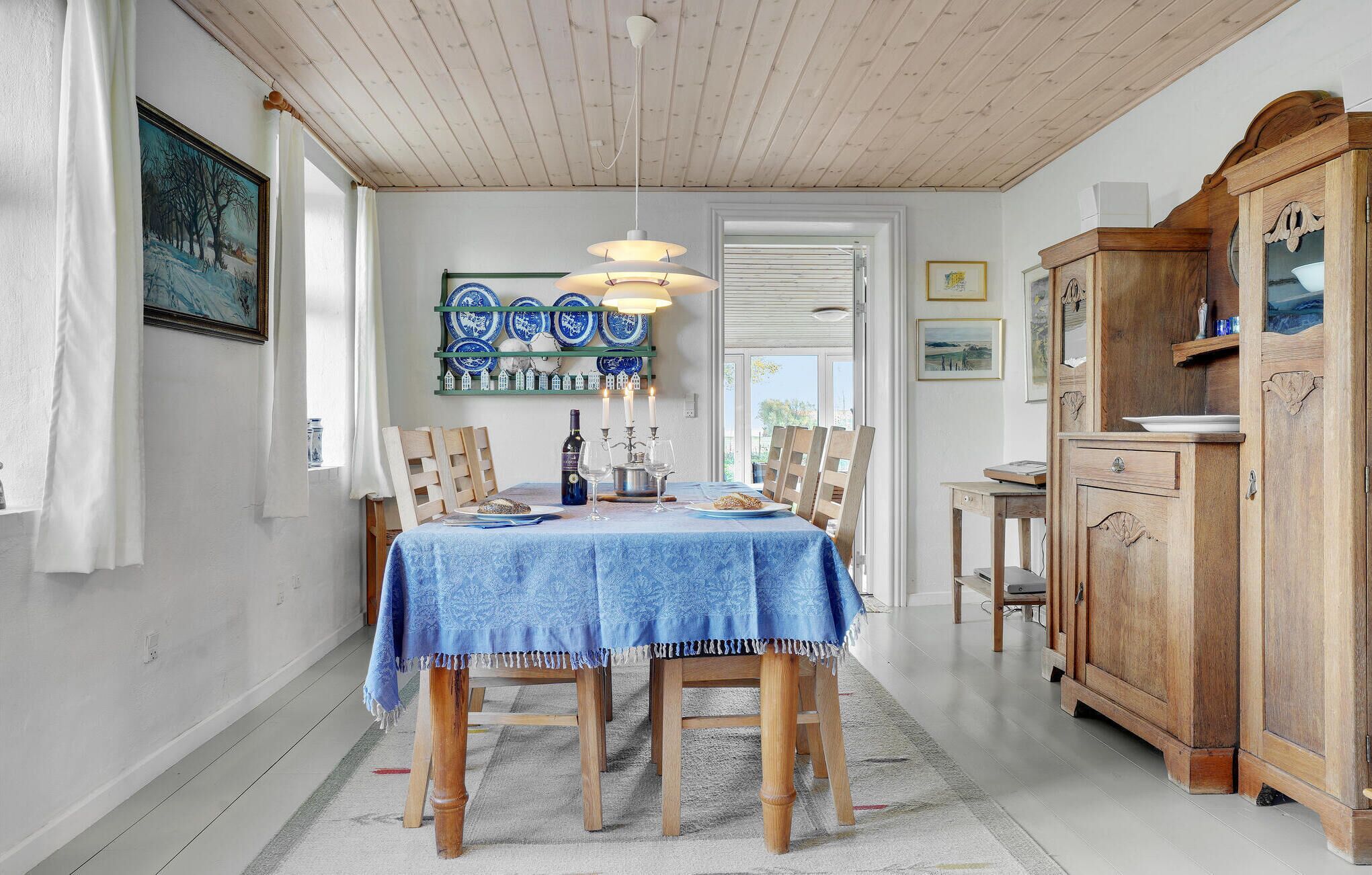 A dining area with a table set for four, wooden chairs, a blue tablecloth, and a decorative plate rack.