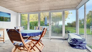 Un patio techado con mesa y sillas, puertas correderas de vidrio grandes y vistas al exterior.