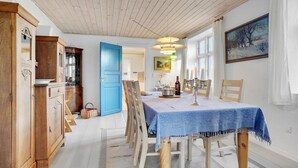 Un comedor con una mesa dispuesta para cuatro, sillas de madera, mantel azul y un cuadro en la pared.