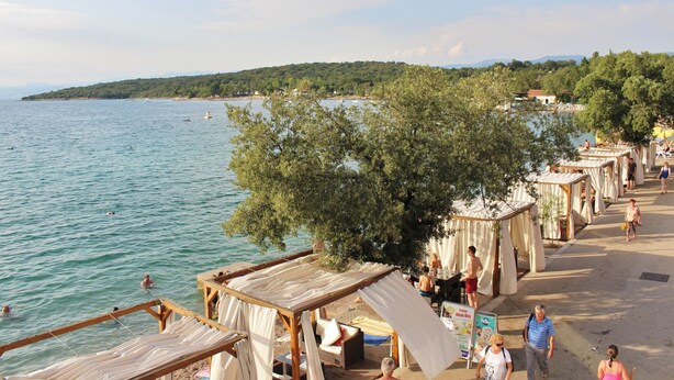 A beachside area with wooden structures, some with canopies, overlooking a calm sea.