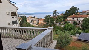 A residential area with a balcony, stone flooring, and a view of the sea and buildings.