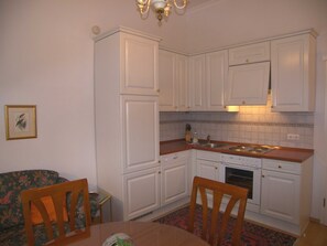Cozinha compacta com armários brancos, mesa de jantar de madeira e cadeiras.