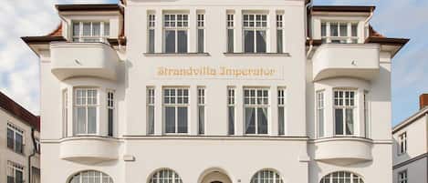 A large, white building with the name "Strandvilla Imperator" on the facade. It has multiple windows, a central entrance with an arch, and balconies on the upper floors.