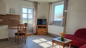 Tunnelmallinen olohuone, jossa on puinen ruokapöytä, punainen sohva ja televisio puisen jalustan päällä.