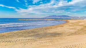 A beach with a rocky breakwater, clear blue sky, and distant mountains. - Cozy home in Málaga with WiFi (Málaga)