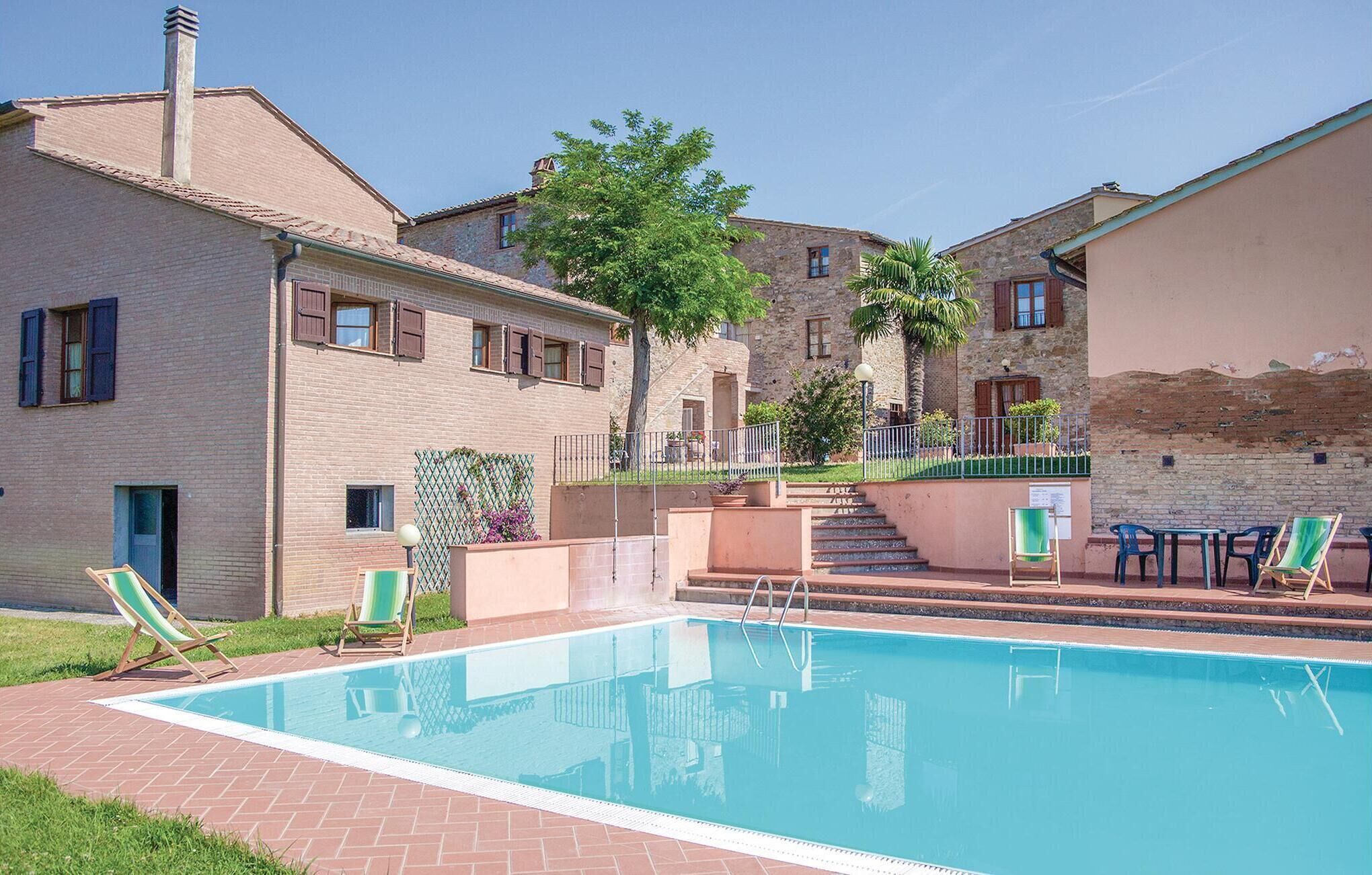 Una piscina con sillas de descanso, un edificio de ladrillo y una escalera que lleva a un balcón.
