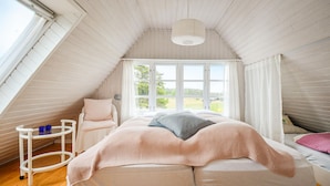 Ein gemütliches Schlafzimmer im Dachgeschoss mit einem großen Fenster, einem Bett, einem Sessel und einem kleinen Tisch.