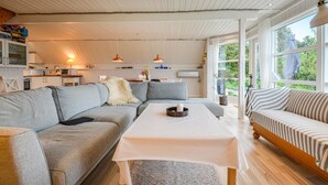 Ein gemütliches Wohnzimmer mit einer Eckcouch, einem kleinen Tisch und einem Fenster mit Blick auf Grünflächen.