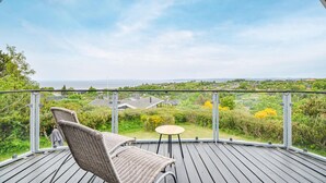 Ein Balkon mit Korbmöbeln, einem kleinen runden Tisch und Blick auf eine Küstenlandschaft.