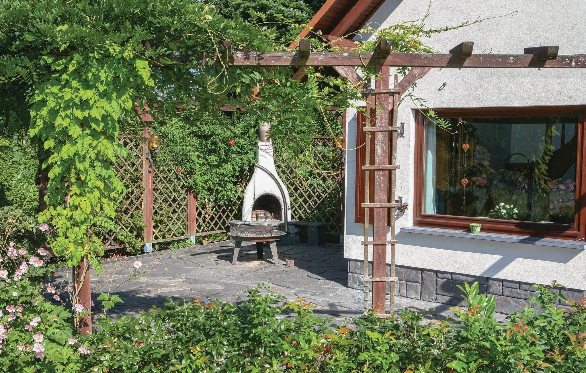 Une terrasse en pierre avec un four à bois, entourée d’une végétation luxuriante et agrémentée d’une pergola en bois.