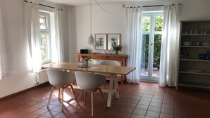 A dining area with a wooden table, two chairs, a white radiator, a ceiling fan, and a view of the garden through a glass door. - Vacation home 1 - Holiday homes Michaelis 1 to 4 in Quilitz (Rankwitz)