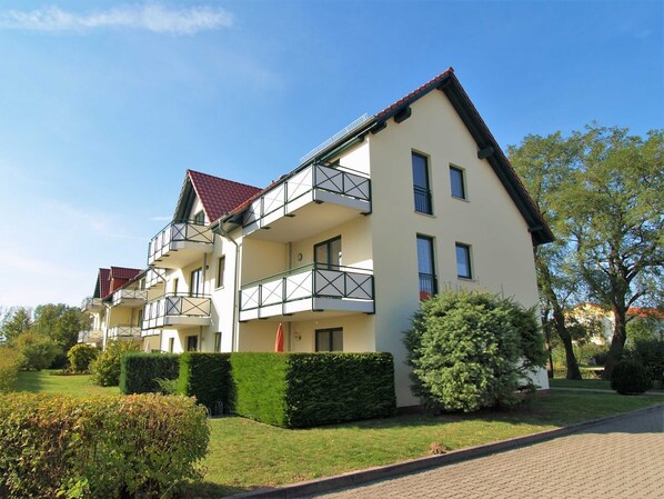 A multi-story residential building with balconies, a red-tiled roof, and a well-maintained garden.