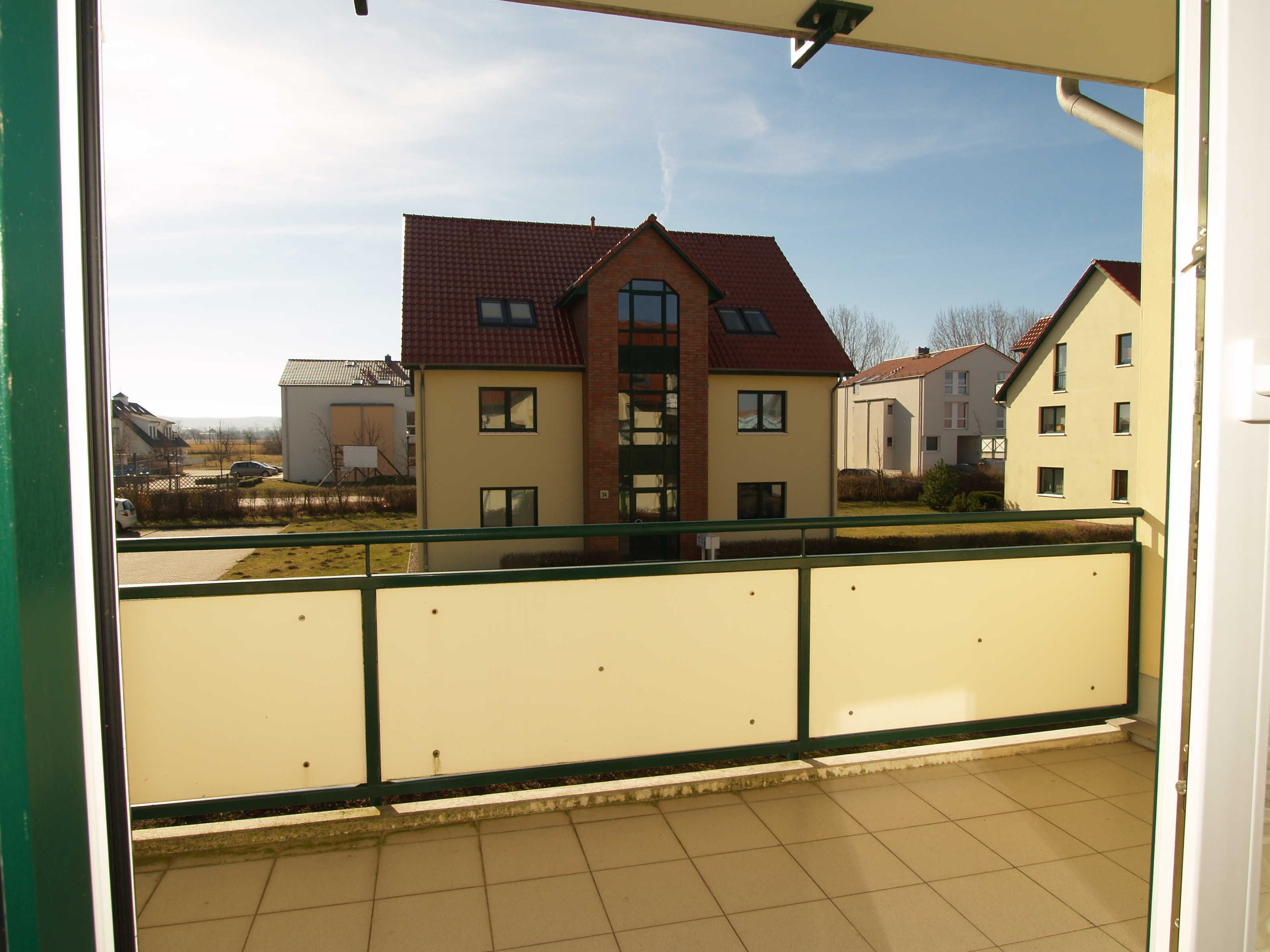 Ein Balkon mit Blick auf ein Wohngebäude, das ein rotes Dach und eine beige Fassade sowie viele Fenster hat.