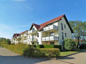 Ein mehrstöckiges Wohngebäude mit Balkonen, einem roten Ziegeldach und einem gepflasterten Zugangsweg.