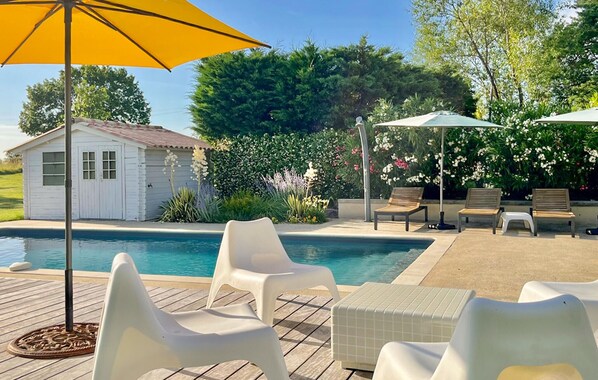 Un espace piscine avec des chaises en plastique blanches, une terrasse en bois et un petit abri de jardin.