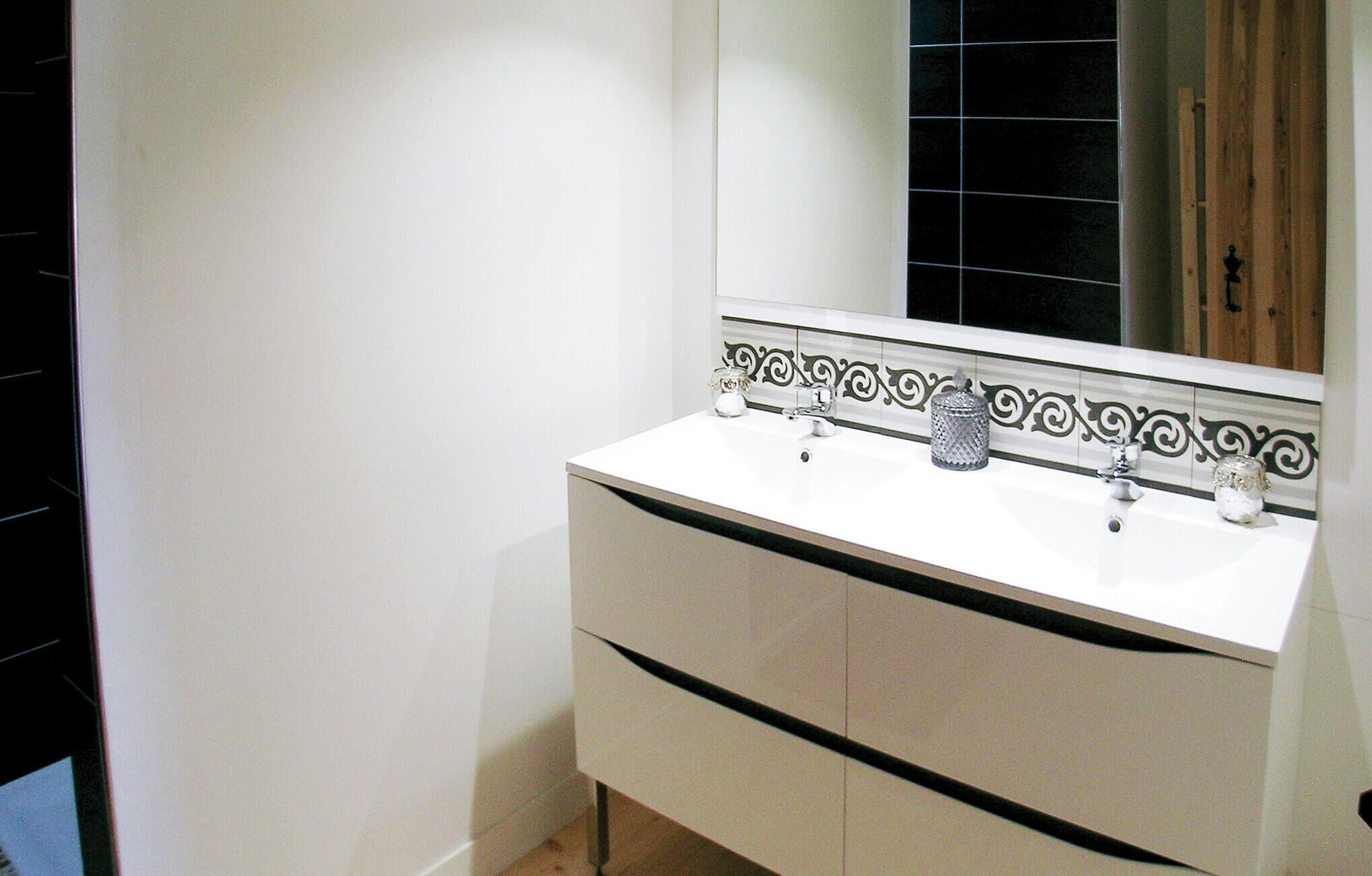 Un baño con un lavabo blanco, dos grifos, un espejo sobre el lavabo y un borde decorativo de azulejos.