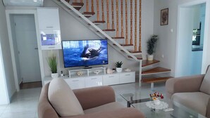 A living room with a TV, two sofas, a glass coffee table, a staircase, and a kitchen in the background. - Holiday home with garden and barbecue (Balatonsz��rszó)