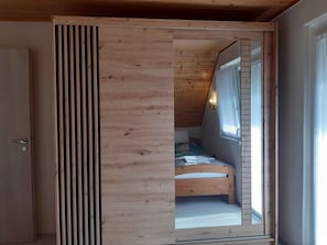 A room with a slanted ceiling, a bed with a checkered bedspread, and a window with curtains.