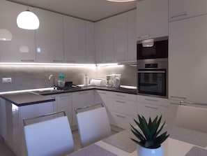 A modern kitchen with white cabinets, a built-in oven, and a coffee maker.