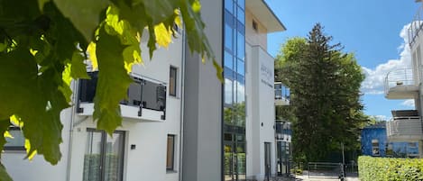 En modern byggnad med en fasad av glas, en stenlagd innergård och en häck längs sidan.