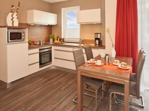 Une cuisine compacte équipée d’un four à micro-ondes, d’un four traditionnel et d’un coin repas avec une table dressée pour deux personnes.