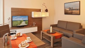 Un salon moderne avec une télévision, un canapé et un coin repas avec une table mise pour deux personnes.