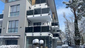 Un immeuble à plusieurs étages, doté de balcons, de grandes fenêtres et entouré d’un paysage enneigé.