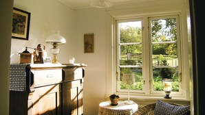 Une pièce avec une grande fenêtre, une commode en bois, une lampe et une chaise en osier.