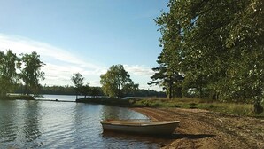 Un bateau sur un lac paisible, avec une rive sablonneuse et des arbres en arrière-plan.