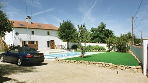 Una casa con piscina, un coche aparcado adelante y un césped bien cuidado.