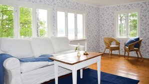 A room with a white sofa, a wooden coffee table, two wicker chairs, and large windows with floral wallpaper. - Cozy home in Gislaved with house sea view (Gislaved)