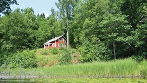 A red house surrounded by dense green trees and a body of water with lily pads. - Cozy home in Gislaved with house sea view (Gislaved)