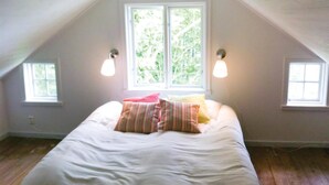 A bedroom with a sloped ceiling, a large bed with white bedding, two wall-mounted lamps, and two windows with a view of greenery. - Cozy home in Gislaved with house sea view (Gislaved)