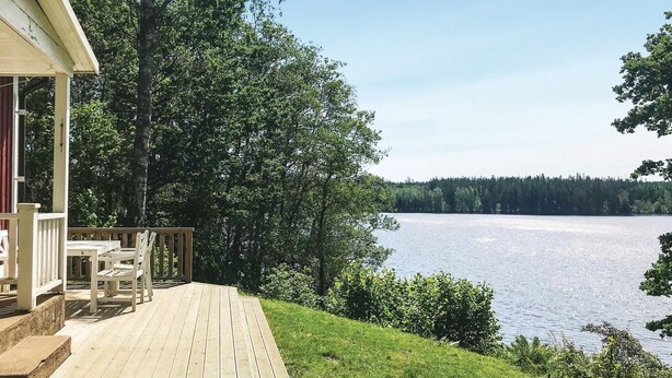 A wooden deck with outdoor furniture overlooking a lake, surrounded by trees. - Cozy home in Gislaved with house sea view (Gislaved)
