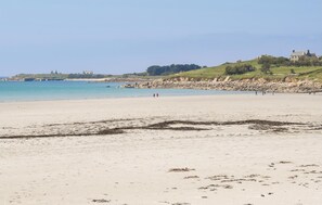 Uma praia com vista clara para o mar, um litoral rochoso e uma colina com um edifício no topo.