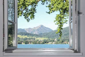 An open window with a view of a lake, mountains, and a village.