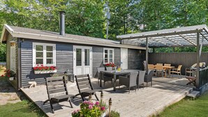 Une terrasse en bois avec un patio couvert, une table à manger avec des chaises et un barbecue.