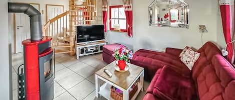 Een woonkamer met een televisie, rode bank, houten trap en een open haard.