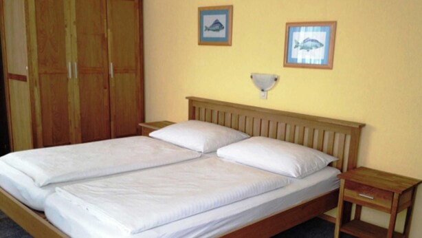 A double bed with white linens, a wooden headboard, two bedside tables, and a wardrobe.