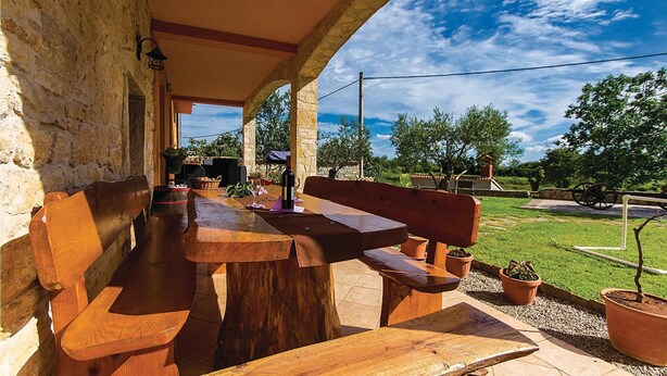Un patio al aire libre con bancos y mesas de madera, muros de piedra y vistas al campo.