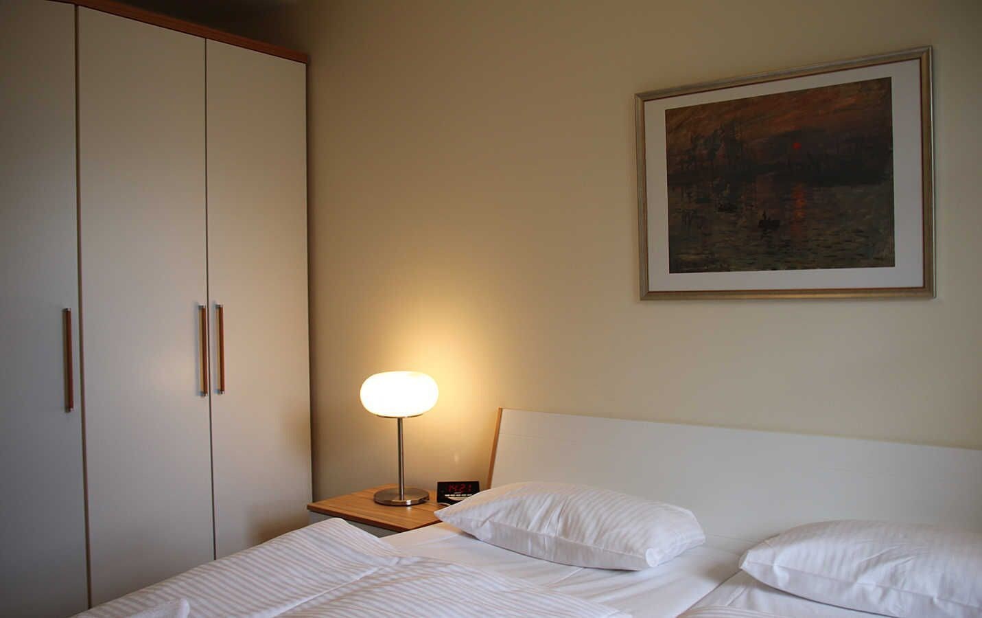 Een hotelkamer met een bed, een nachtkastje met een lamp, een kledingkast en een fotokader aan de muur.
