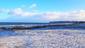 A coastal landscape with a clear sky, a sandy beach, and a distant shoreline.