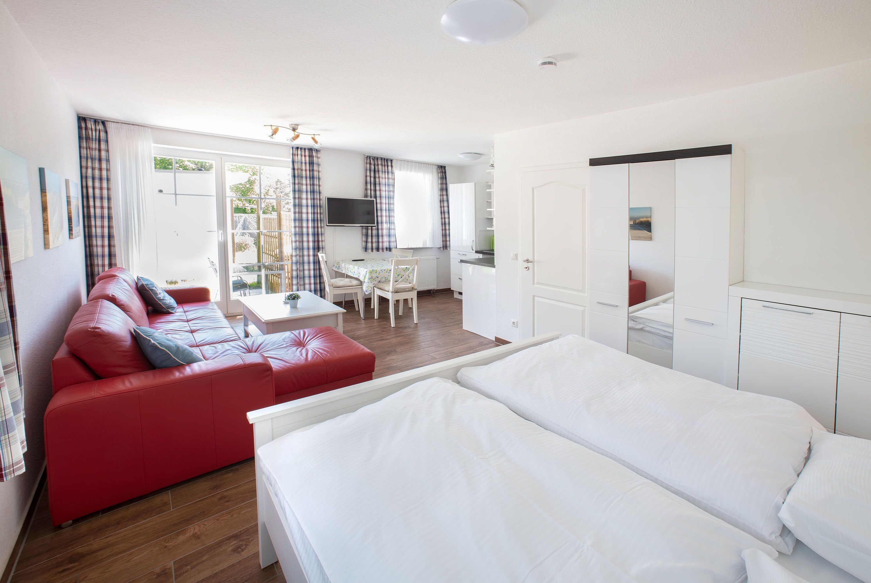 A hotel room with a red sofa, a bed, a desk, and a kitchenette.