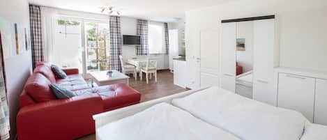 Une chambre d’hôtel avec un canapé rouge, un lit, un bureau et une kitchenette.