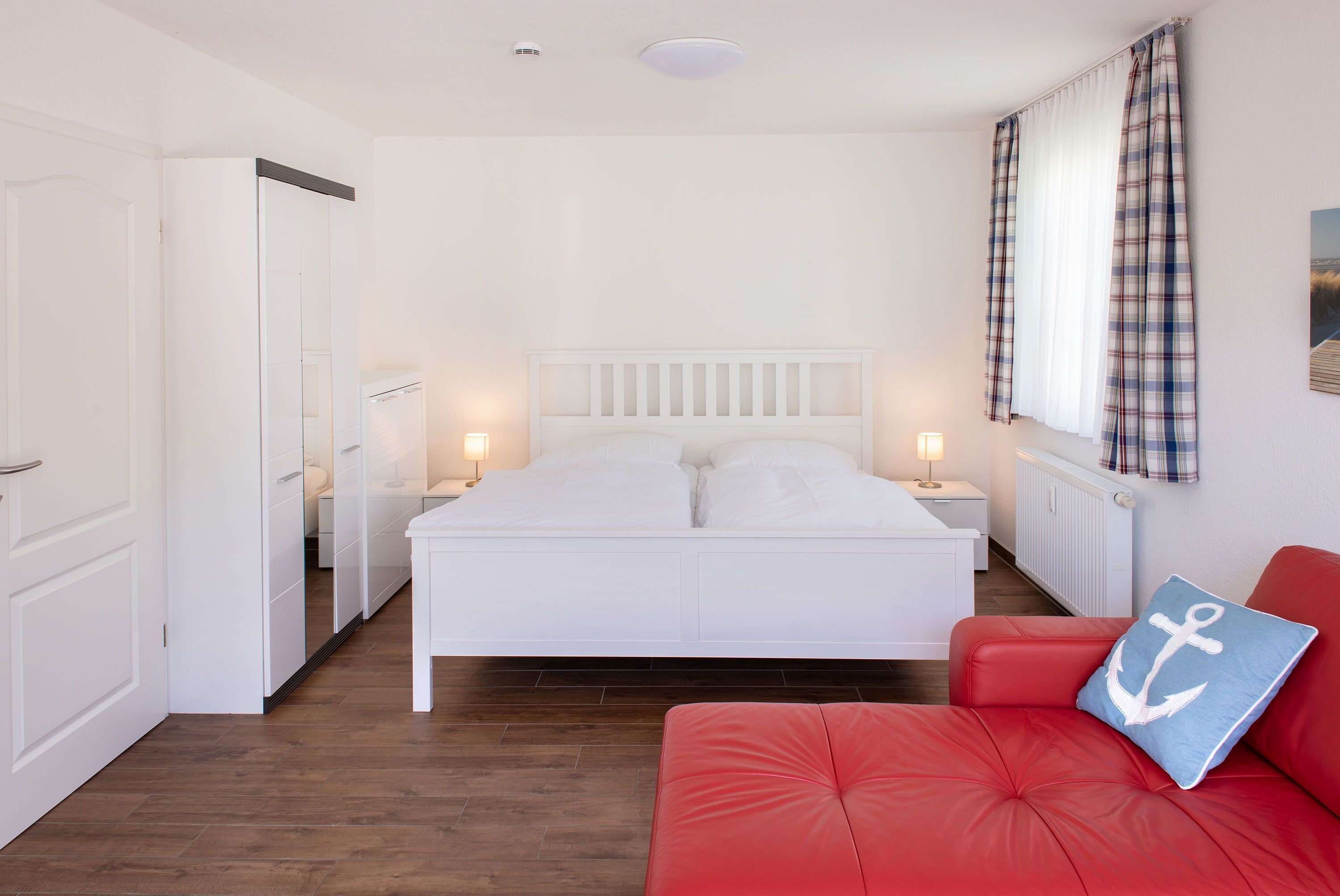 A bedroom with a bed, a red sofa, a nightstand, and a window with curtains.