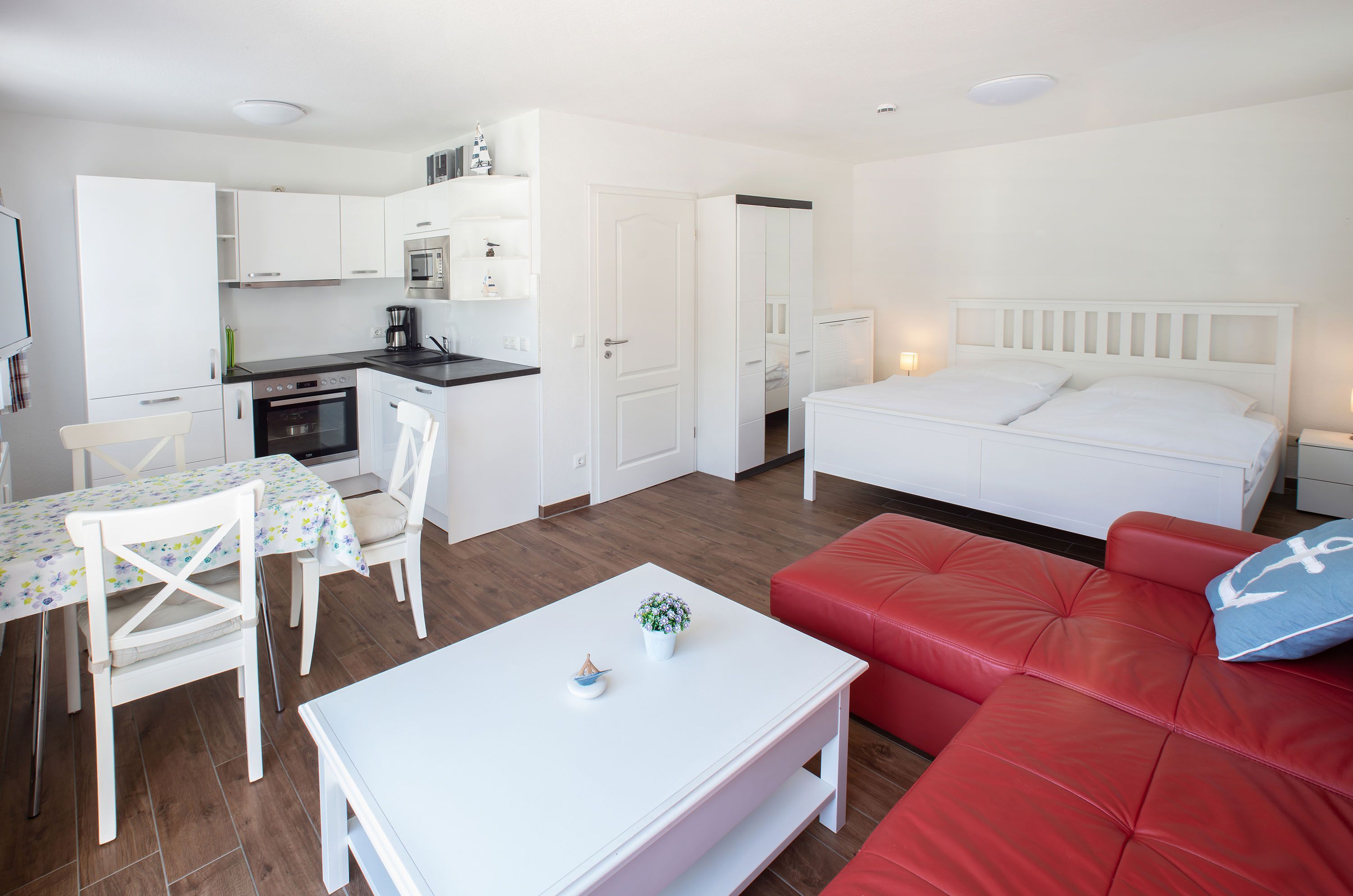 A compact living space with a kitchenette, a dining area, a red sofa, and a bed.