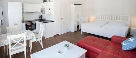 A compact living space with a kitchenette, a dining area, a red sofa, and a bed.