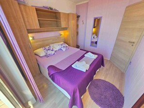 A bedroom with a bed, a wooden wardrobe, a mirror, and a small round table.